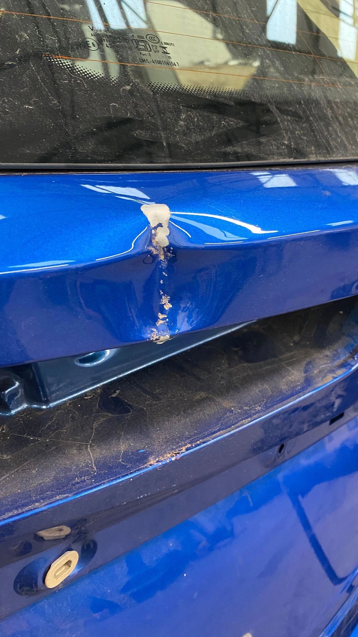 Close-up of a stone chip in blue car paint exposing the layer beneath