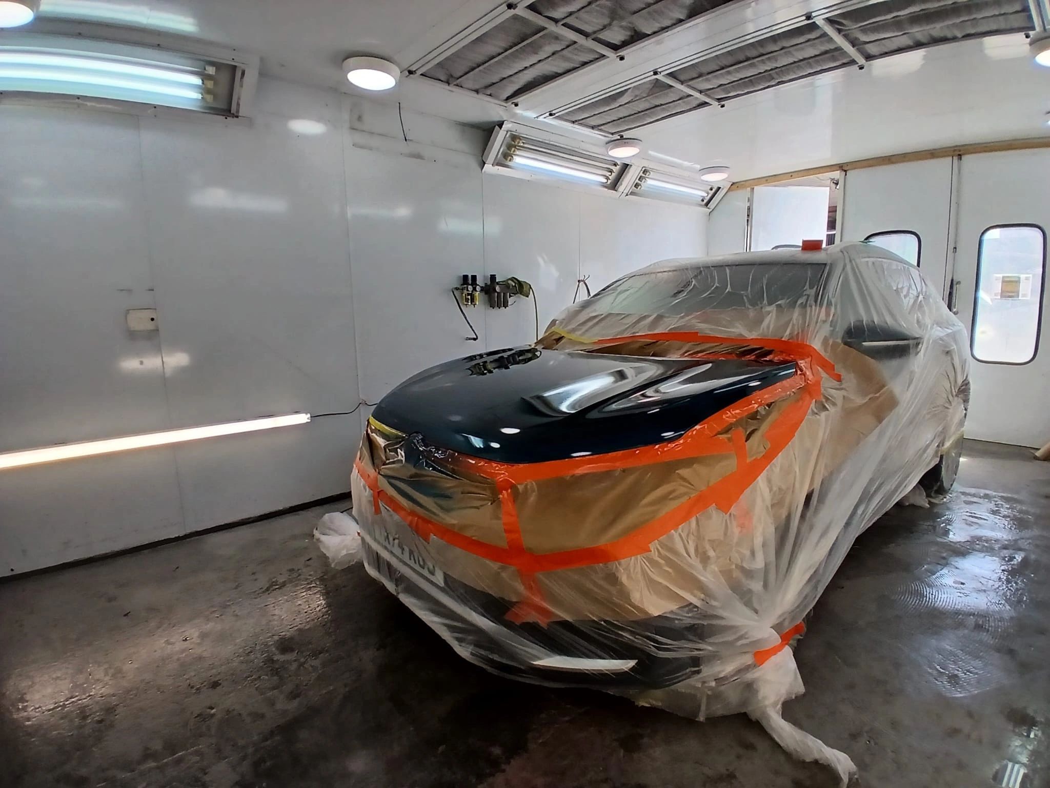 A freshly sprayed car panel curing under the lights in a spray booth