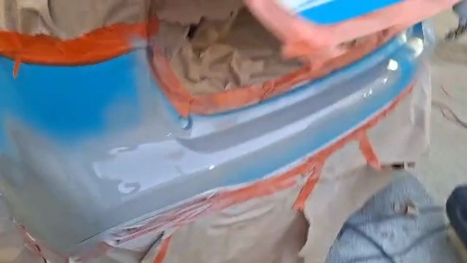 Blue paint being sprayed onto a car bumper during a scratch repair